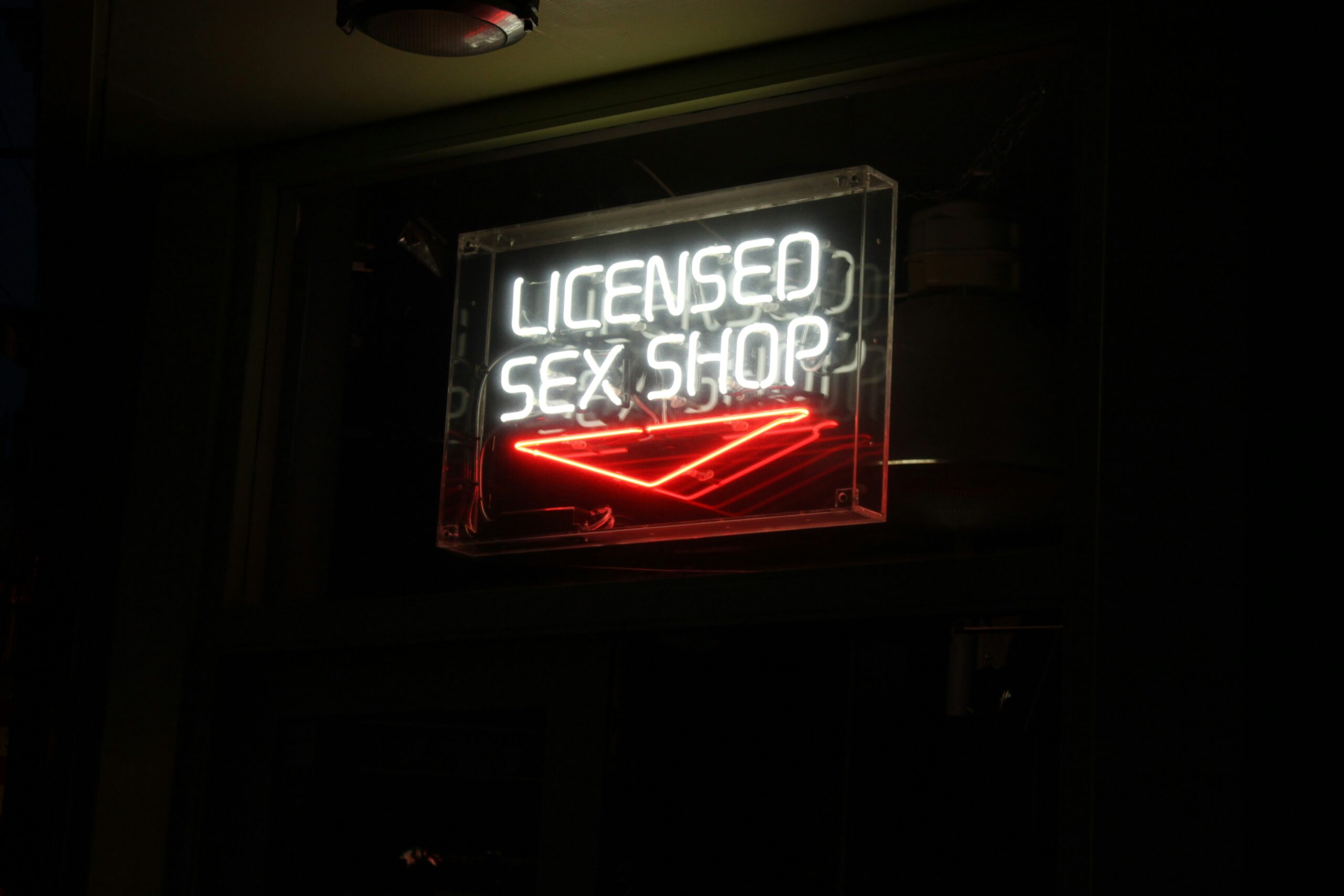 white neon sign that says "licensed sex shop" and a red neon arrow pointing down