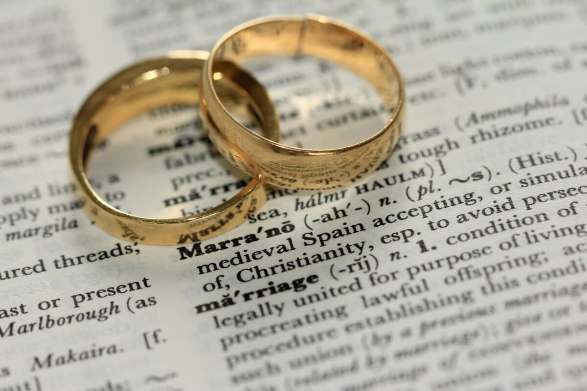 Two gold wedding rings placed on a dictionary page, with the word 'marriage' prominently in focus, symbolizing love and commitment.