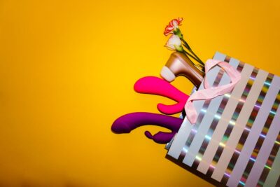 A shopping bag with adult toys, flowers, and a high heel shoe on a vibrant yellow background.
