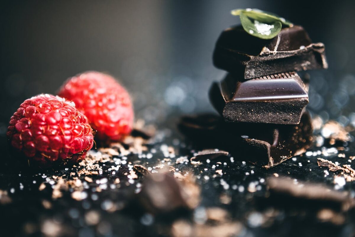 Stacked dark chocolate pieces with fresh raspberries, sprinkled with sea salt and cocoa shavings.