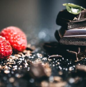 Stacked dark chocolate pieces with fresh raspberries, sprinkled with sea salt and cocoa shavings.