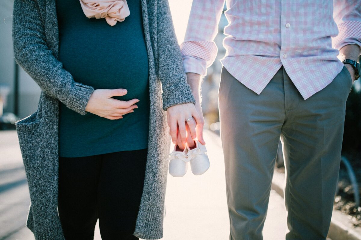 A pregnant woman and her partner holding baby shoes, symbolizing their upcoming parenthood.