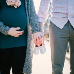 A pregnant woman and her partner holding baby shoes, symbolizing their upcoming parenthood.