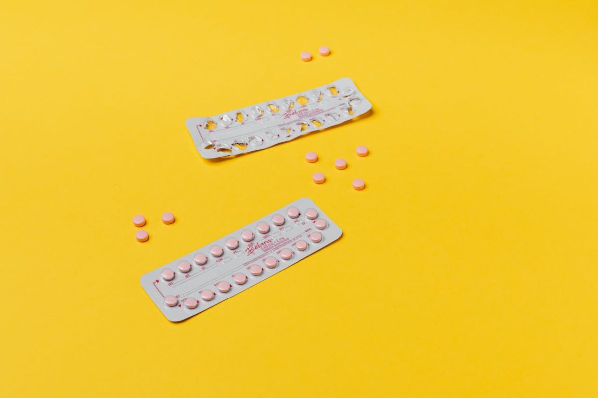Two packs of birth control pills with scattered tablets on a bright yellow background.