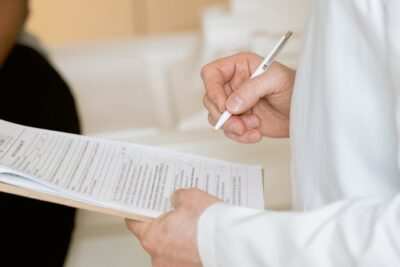 A doctor reviewing and signing a medical form on a clipboard.