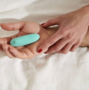 Teal bullet vibrator resting on a partner's palm, perfect for intimate shared moments in bed.