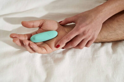 Teal bullet vibrator resting on a partner's palm, perfect for intimate shared moments in bed.