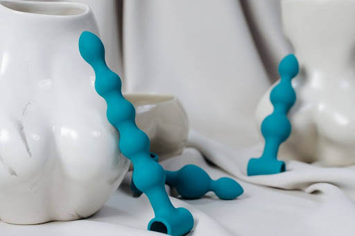 Teal silicone anal beads displayed against white ceramic vases and soft draped fabric, highlighting a stylish and modern aesthetic.