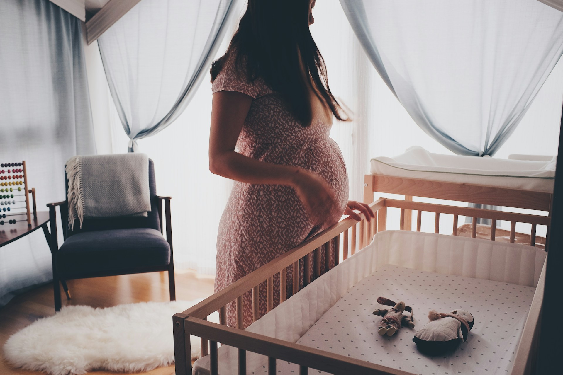 Pregnant woman standing by a crib. Explores common filipino superstitions about pregnancy and preparing the home for a new arrival.