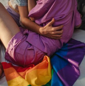 Warm moment of a same-sex couple hugging indoors with a rainbow flag, symbolizing love and unity.
