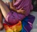 Warm moment of a same-sex couple hugging indoors with a rainbow flag, symbolizing love and unity.