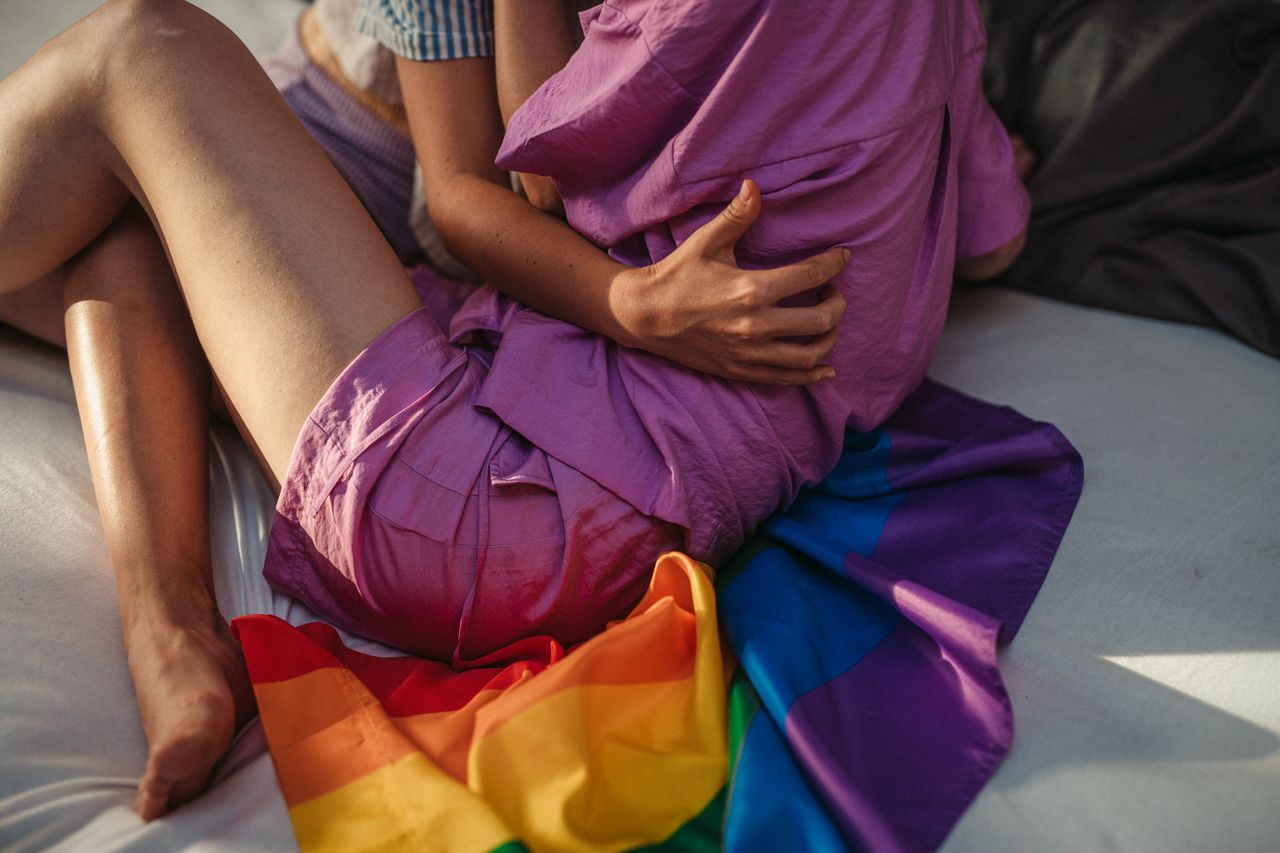 Warm moment of a same-sex couple hugging indoors with a rainbow flag, symbolizing love and unity.