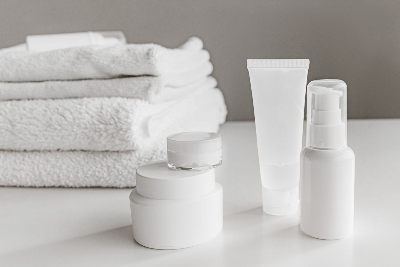 Clean white self care essentials including cream, lotion, and fresh towels, representing a simple daily intimate hygiene and wellness routine.
